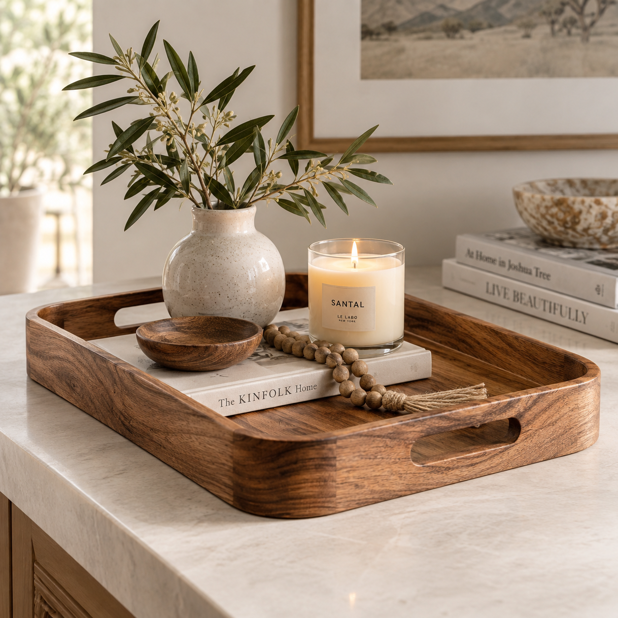 Large wooden tray styled with a ceramic vase, candle, book, and wooden beads