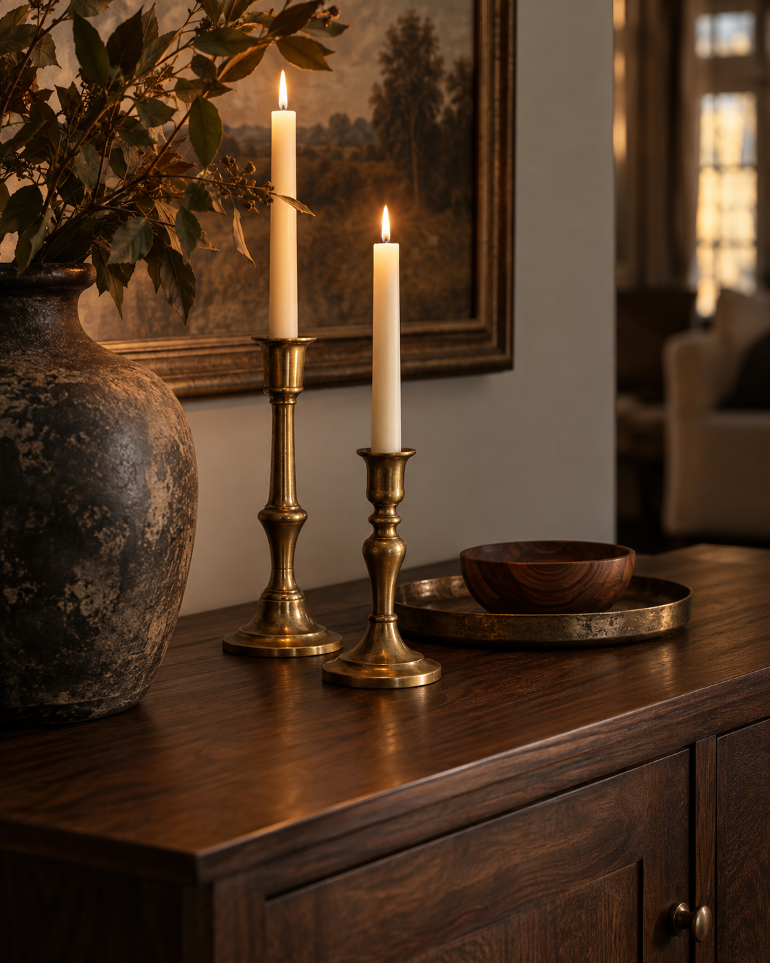 Aged brass candleholders and a wooden bowl arranged on a rich wood sideboard